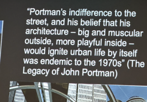 A slide with white text "Portman's indifference to the street, and his belief that his architecture-big and muscular outside, more playful inside-would ignite urban life by itself was endemic to the 1970s" (The Legacy of John Portman)